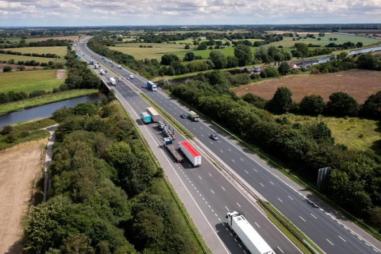 Aerial view of a busy highway in the U.K., showcasing various trucks and vehicles on the road, representing HS Agency's commitment to efficient transportation and logistical solutions across the United Kingdom and Ireland. The surrounding greenery highlights the agency's local roots and dedication to sustainable logistics practices.