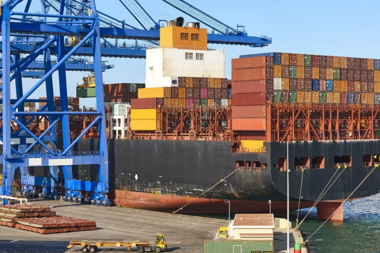 Container ship at a port being loaded and unloaded, showcasing HS Agency's logistical solutions, including shipping, transportation, and warehousing services for efficient supply chain management across the UK and Ireland.